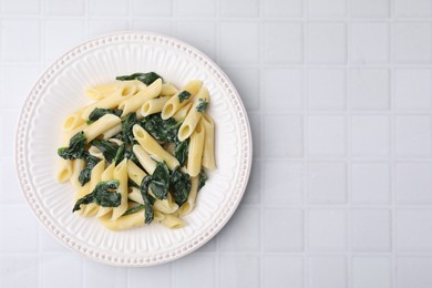 Photo of Tasty pasta with spinach and sauce on white tiled table, top view. Space for text