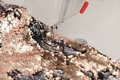 Photo of Sewing machine and beautiful fabric with paillettes indoors, closeup