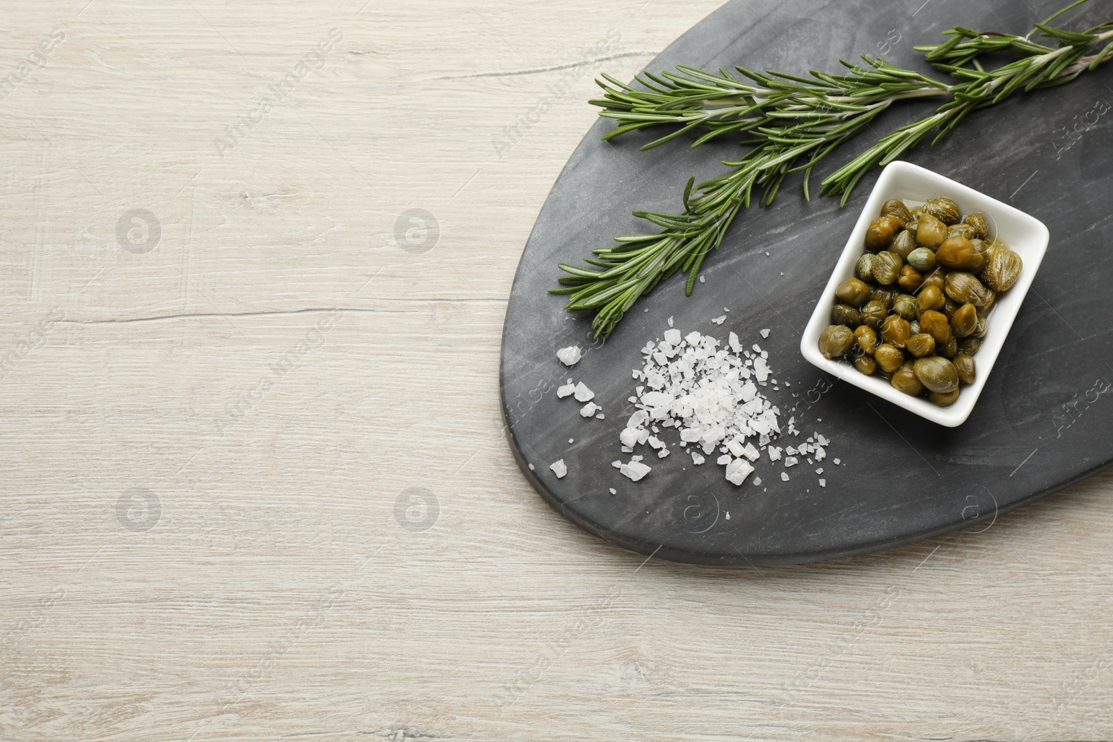 Photo of Delicious pickled capers, salt and rosemary twigs on white wooden table, top view. Space for text