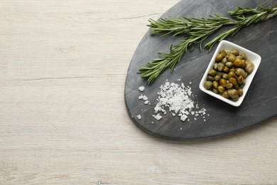 Photo of Delicious pickled capers, salt and rosemary twigs on white wooden table, top view. Space for text