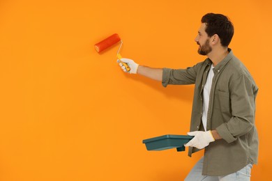 Photo of Designer painting orange wall with roller, space for text