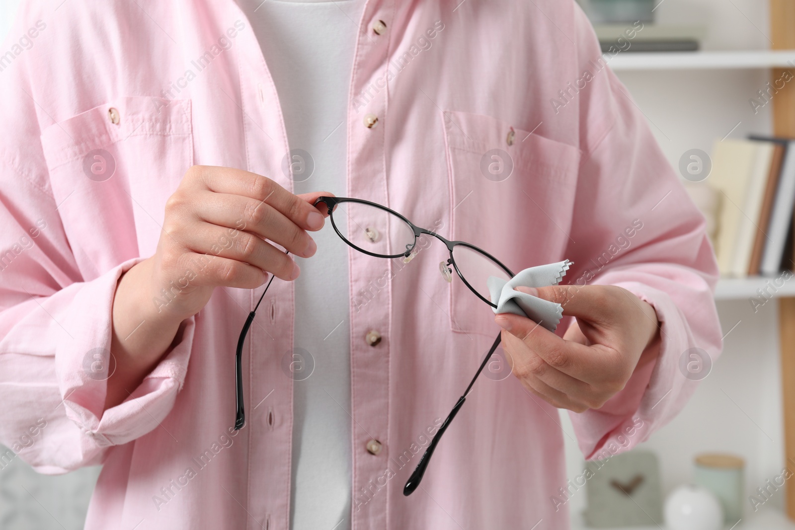 Photo of Woman wiping her glasses with microfiber cloth at home, closeup