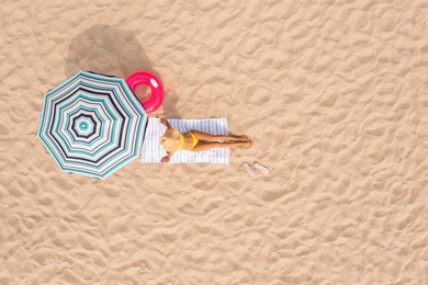 Image of Woman resting under striped beach umbrella at sandy coast, aerial view. Space for text