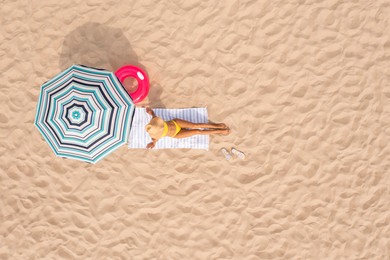 Woman resting under striped beach umbrella at sandy coast, aerial view. Space for text