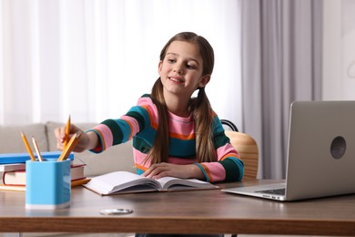 Photo of E-learning. Cute girl using laptop during online lesson at table indoors