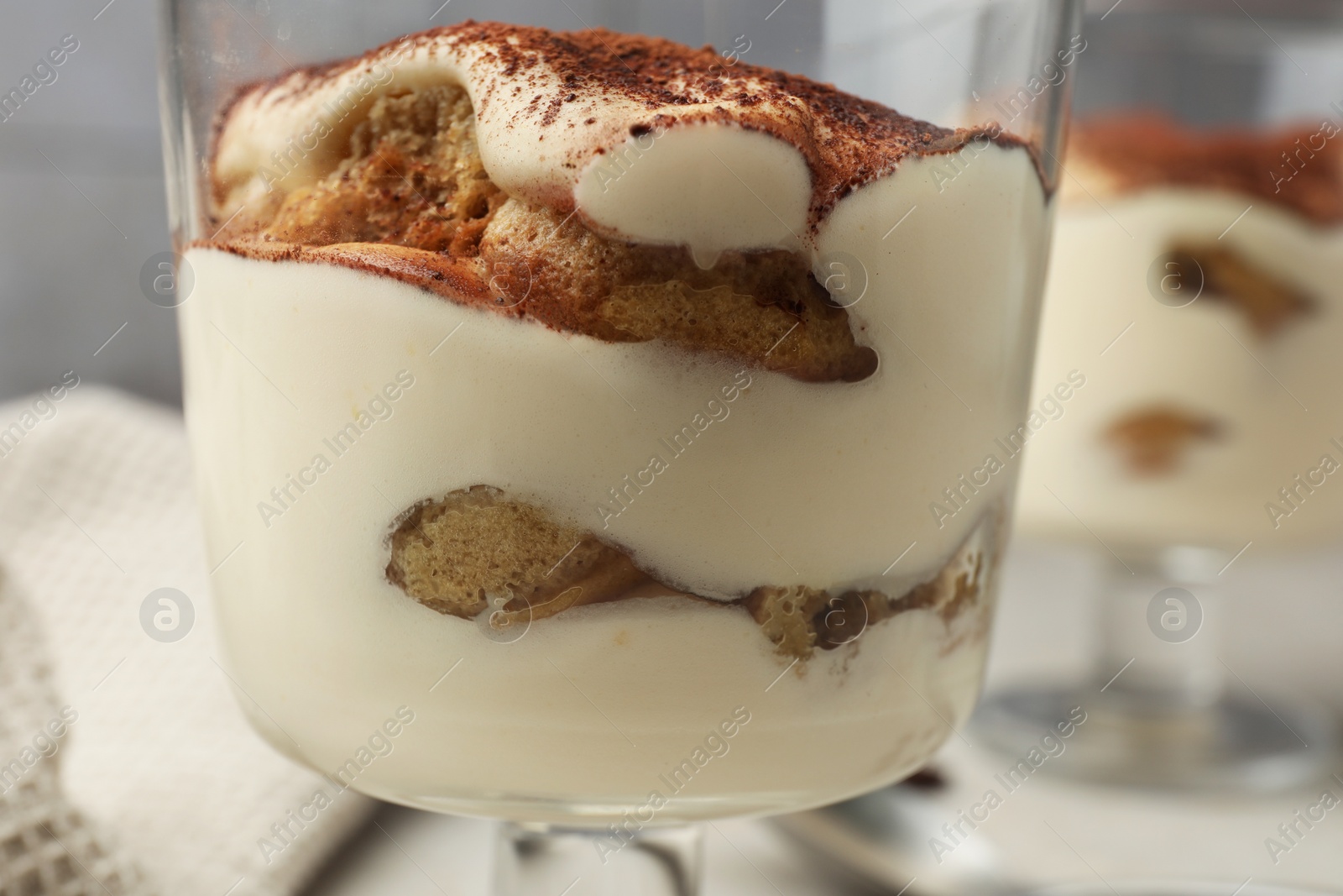 Photo of Delicious tiramisu in glass on blurred background, closeup