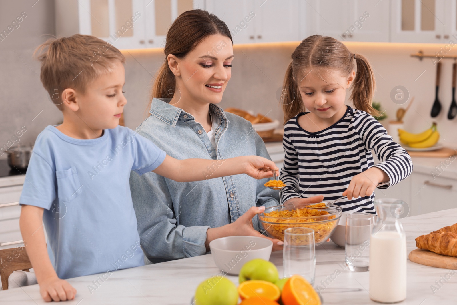 Photo of Mother and her little children having breakfast at table in kitchen