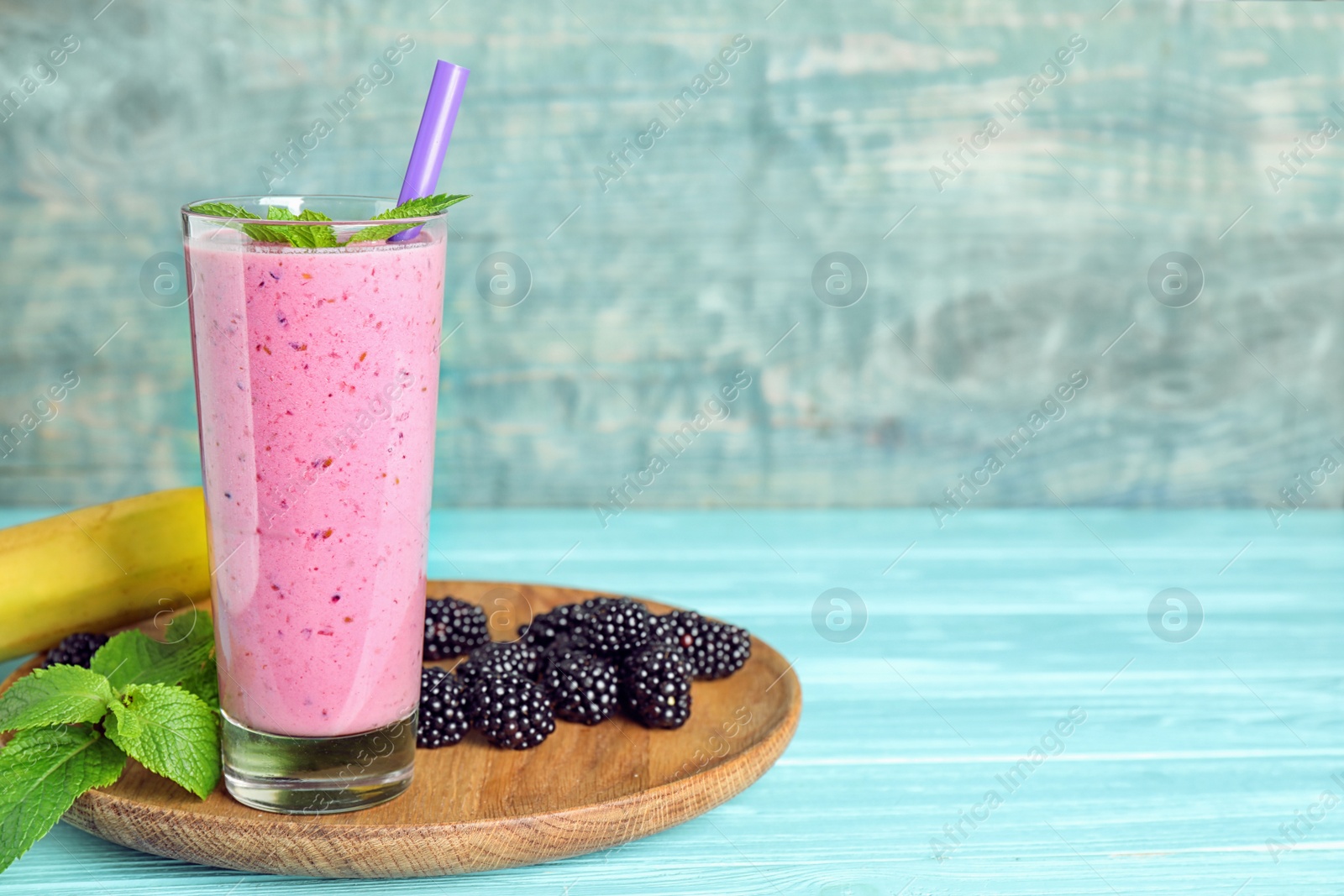 Photo of Delicious blackberry smoothie in glass served on light blue wooden table. Space for text
