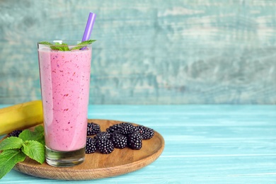 Photo of Delicious blackberry smoothie in glass served on light blue wooden table. Space for text