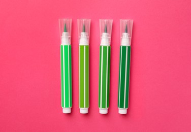 Bright green markers on pink background, flat lay