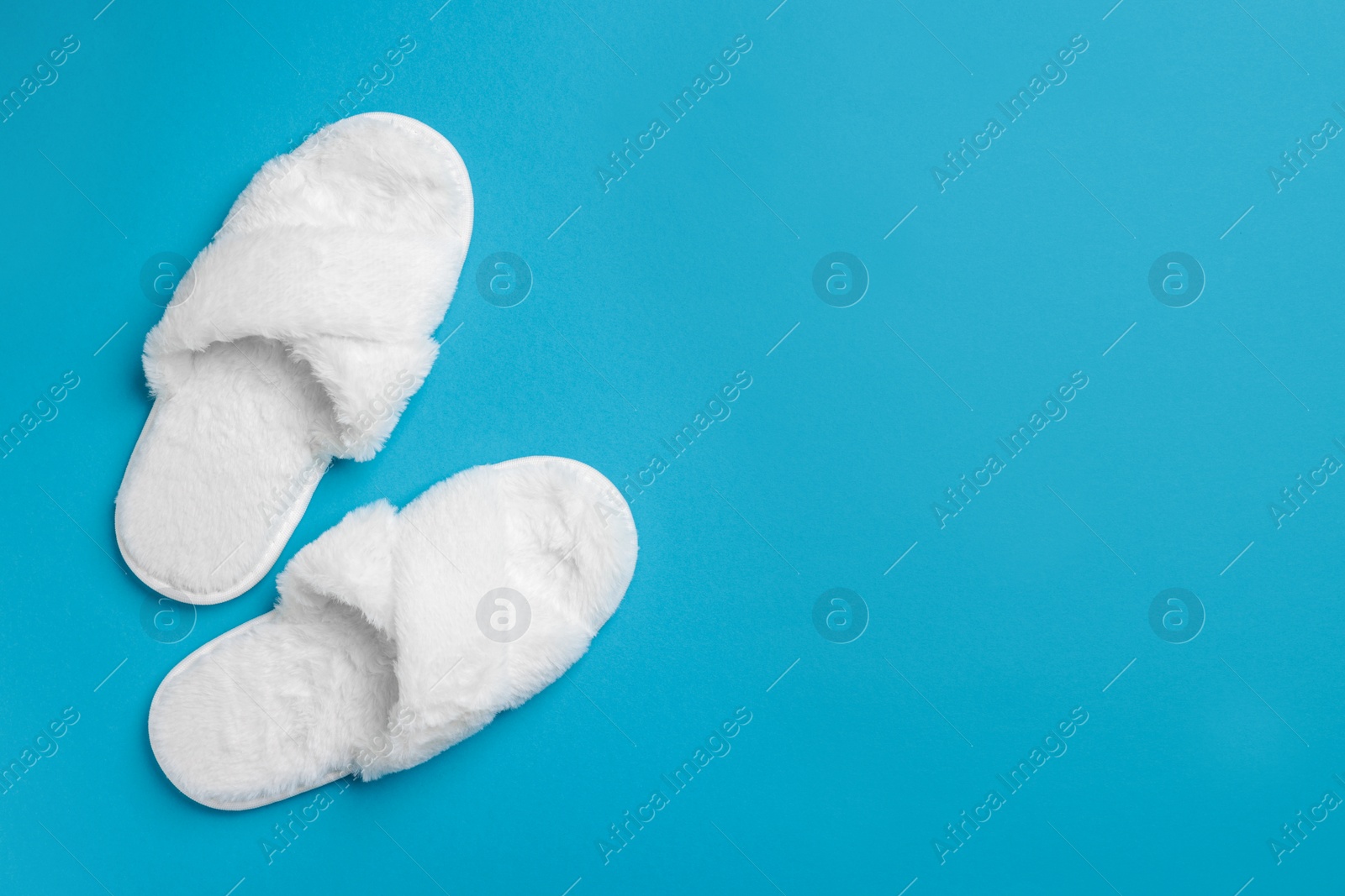 Photo of Pair of soft fluffy slippers on light blue background, top view. Space for text