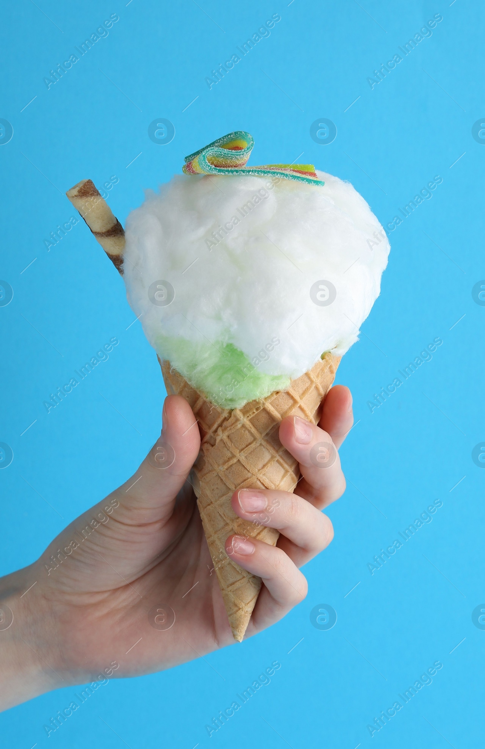 Photo of Woman holding waffle cone with cotton candy on light blue background, closeup