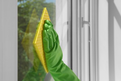 Photo of Woman cleaning window glass with sponge cloth indoors, closeup