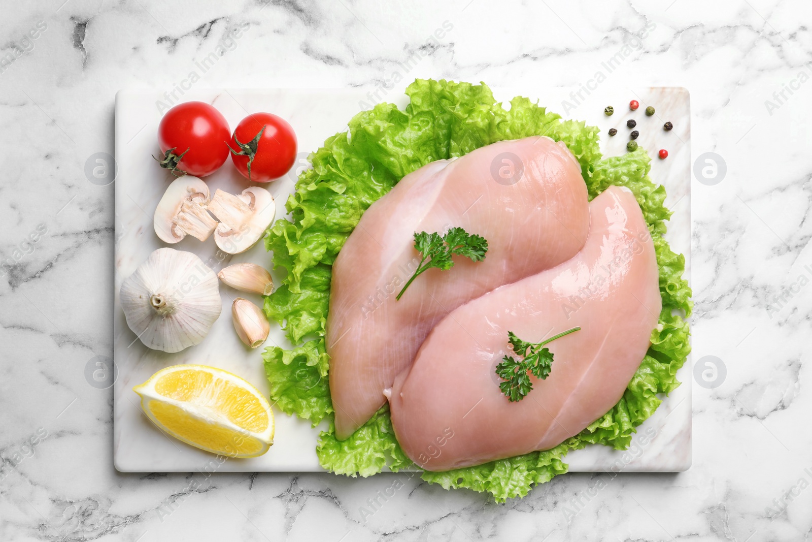 Photo of Board with raw chicken breasts and ingredients on marble background, top view