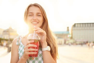 Young woman with refreshing drink on city street. Space for text