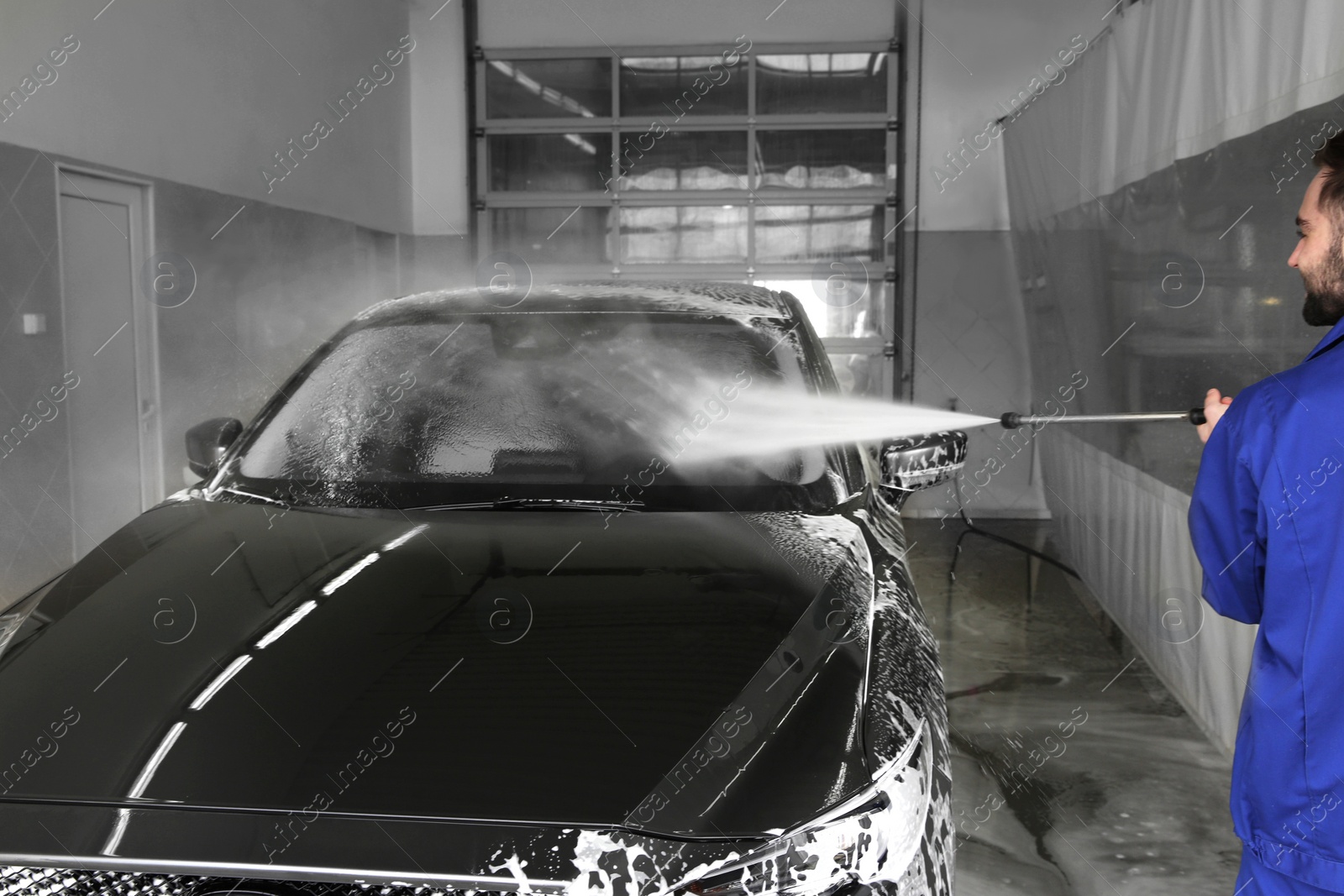 Photo of Worker cleaning automobile with high pressure water jet at car wash