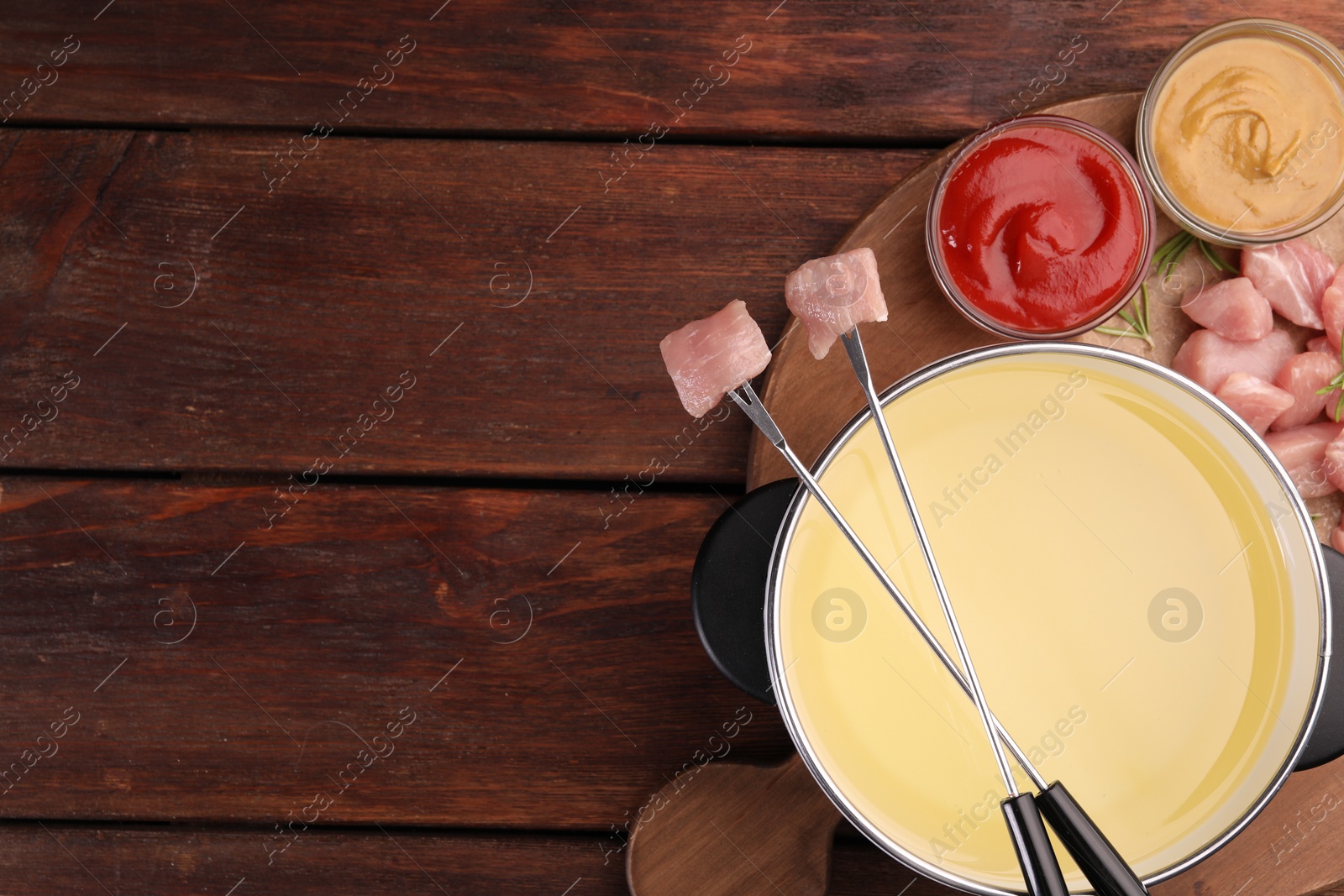 Photo of Fondue pot, forks with pieces of raw meat and sauces on wooden table, flat lay. Space for text