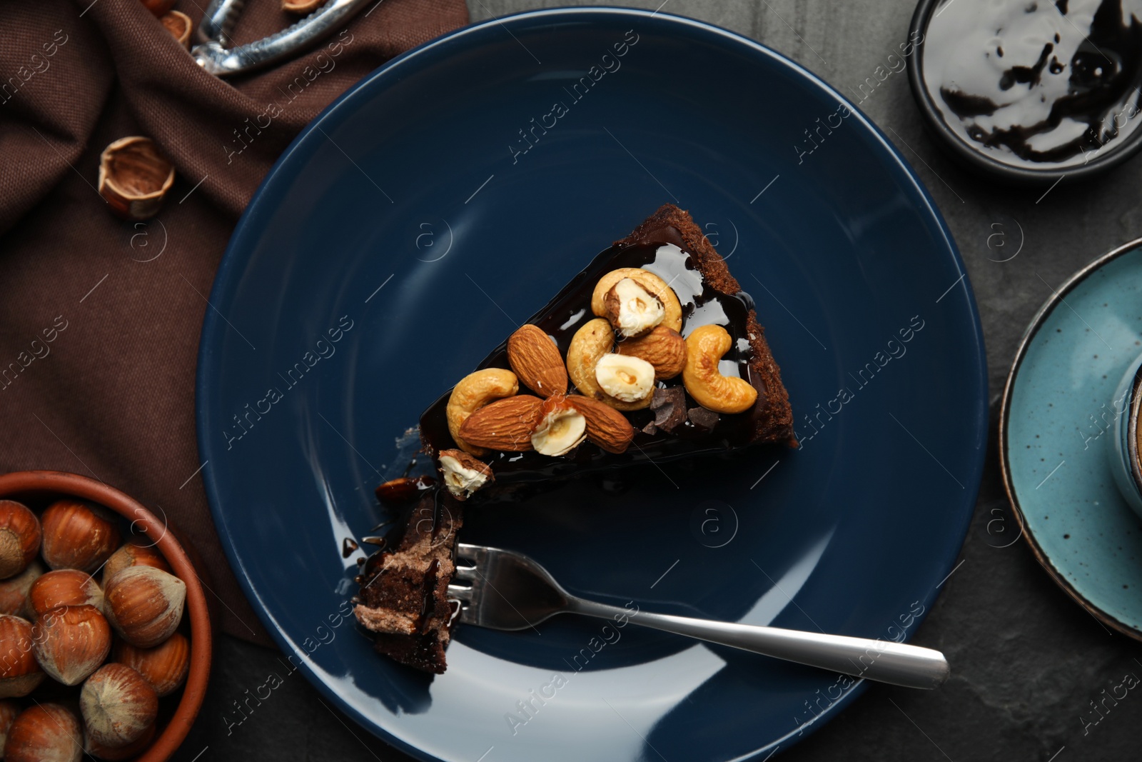 Photo of Piece of tasty homemade chocolate cake with nuts served on black table, flat lay