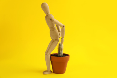 Photo of Wooden human figure and cactus on yellow background. Hemorrhoid problems