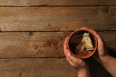 Photo of Donate and give concept. Woman holding bowl with coins and dollar banknotes at wooden table, top view. Space for text