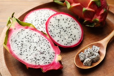 Photo of Wooden plate of delicious cut and whole white pitahaya fruits with spoon on table, closeup