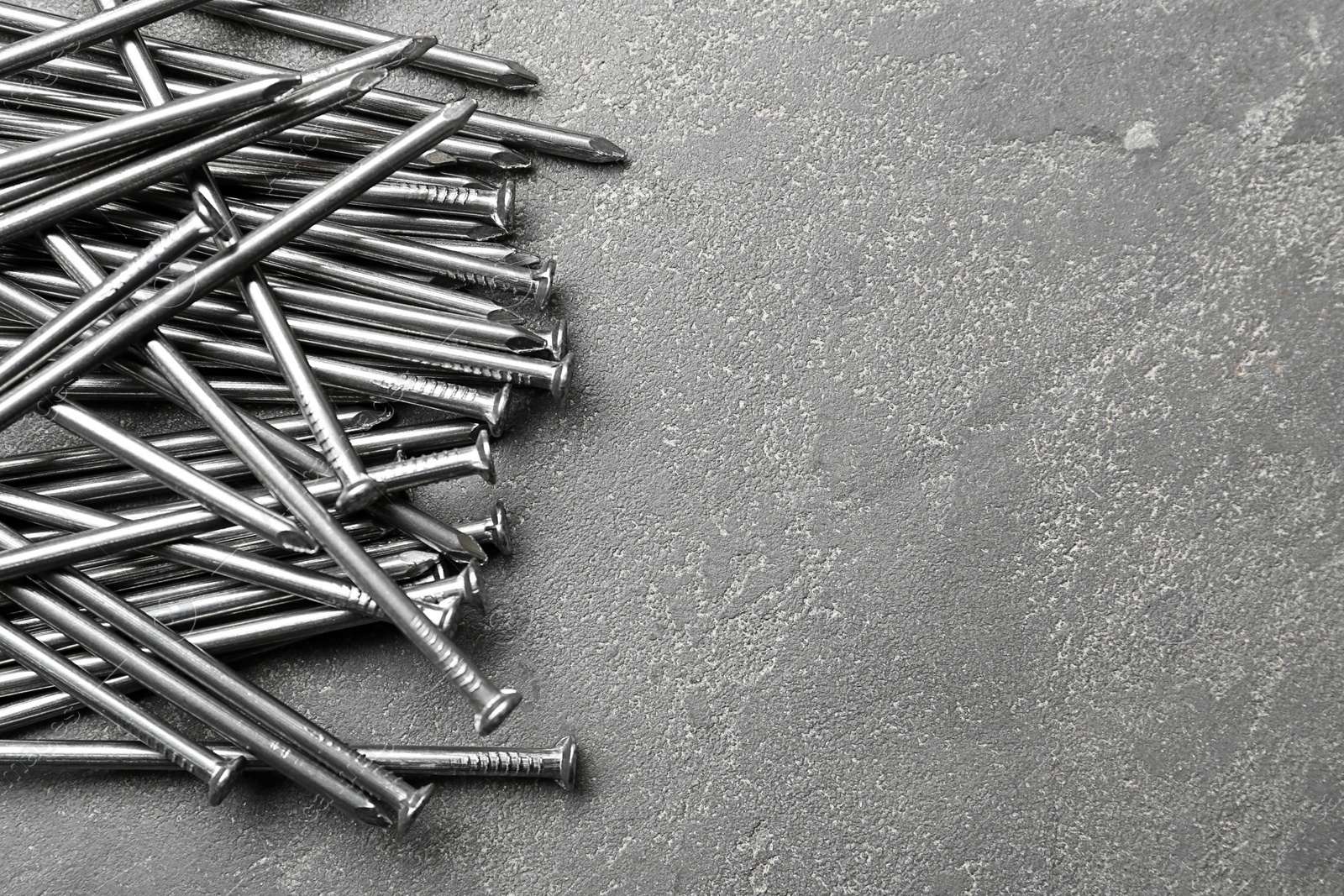 Photo of Pile of metal nails on grey stone background, flat lay. Space for text