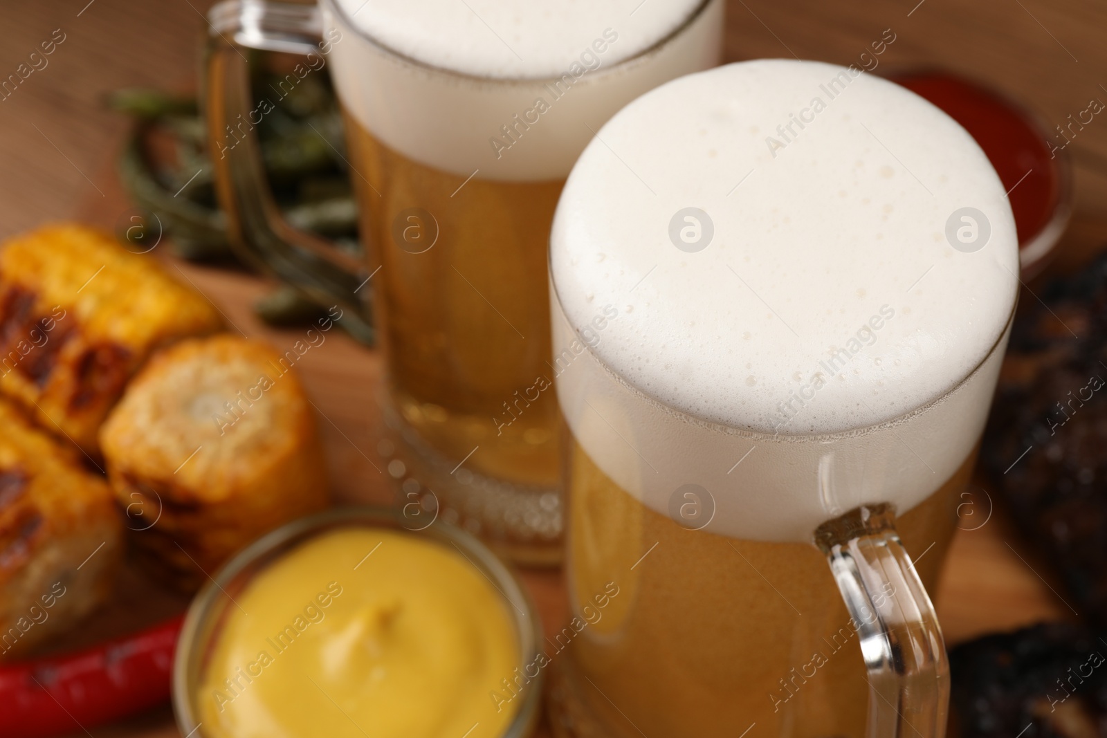 Photo of Mugs of tasty beer and snacks on table, closeup
