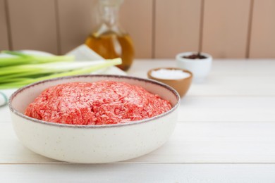 Bowl of raw fresh minced meat on white wooden table, closeup. Space for text