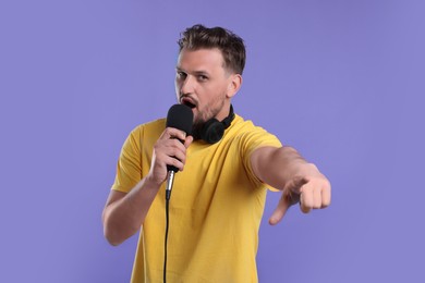 Handsome man with microphone singing on violet background