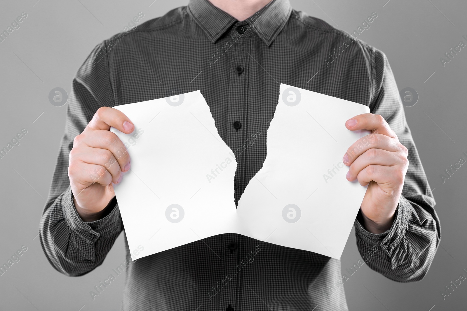 Photo of Man ripping sheet of paper on grey background, closeup. Mockup for design