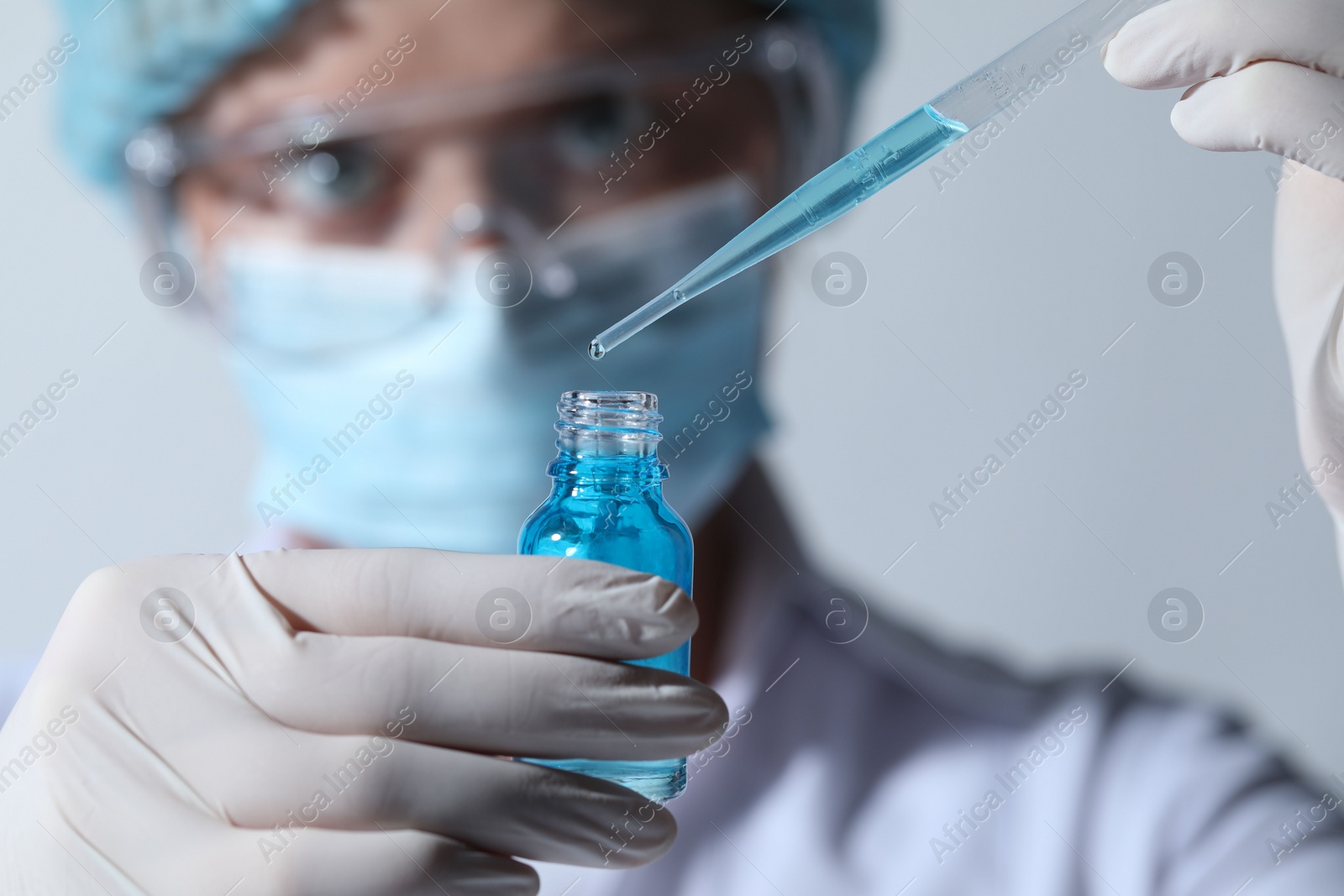 Photo of Scientist dripping liquid from pipette into glass bottle on light background, closeup