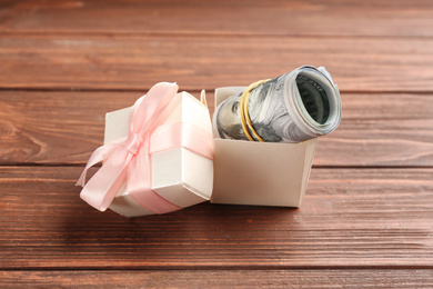 Gift box with dollar bills on wooden table