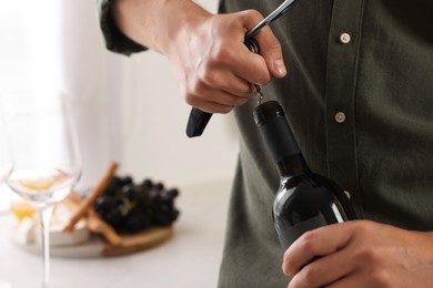 Photo of Romantic dinner. Man opening wine bottle with corkscrew in kitchen, closeup and space for text