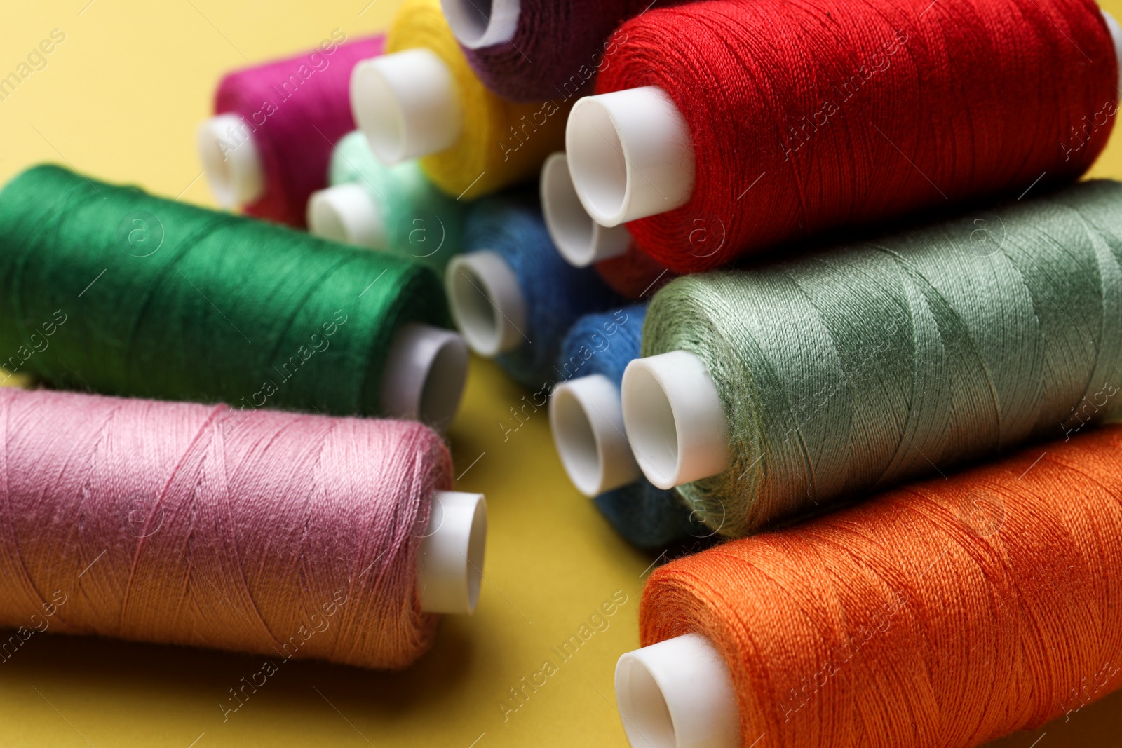 Photo of Different colorful sewing threads on yellow background, closeup