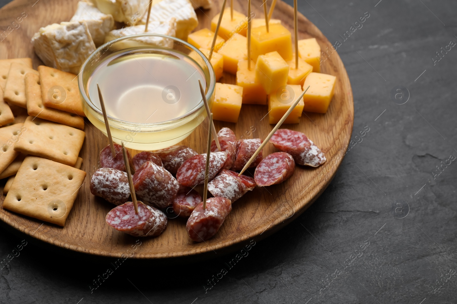 Photo of Toothpick appetizers. Pieces of sausage, cheese and honey on black table