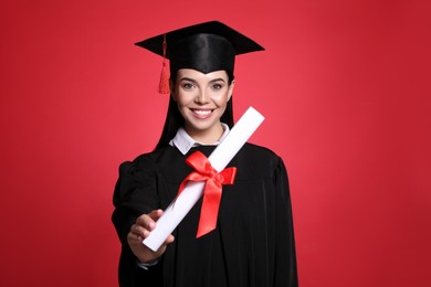 Photo of Happy student with graduation hat and diploma on red background