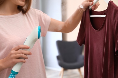 Photo of Young woman steaming her clothes at home, closeup