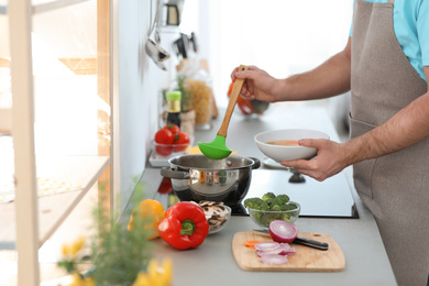 Photo of Young man pouring delicious soup into bowl at home, closeup