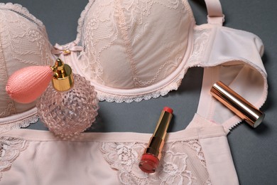 Photo of Elegant beige plus size women's underwear, lipsticks and perfume on grey background, closeup