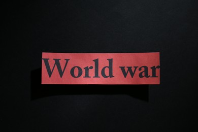 Photo of Paper with words World War on black background, top view