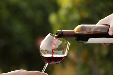 Photo of Woman pouring wine from bottle into glass outdoors, closeup