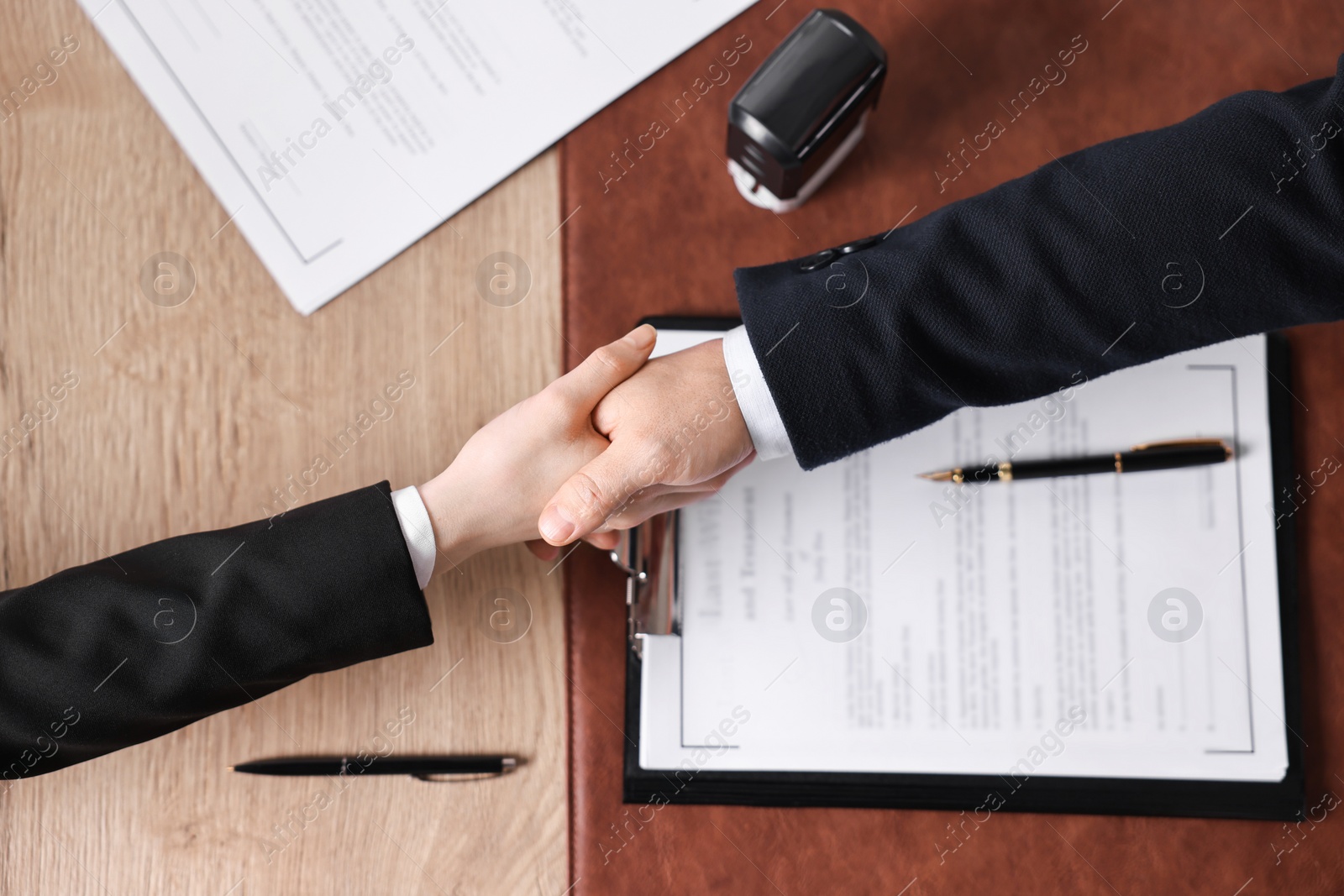 Photo of Notary shaking hands with client at wooden table, top view