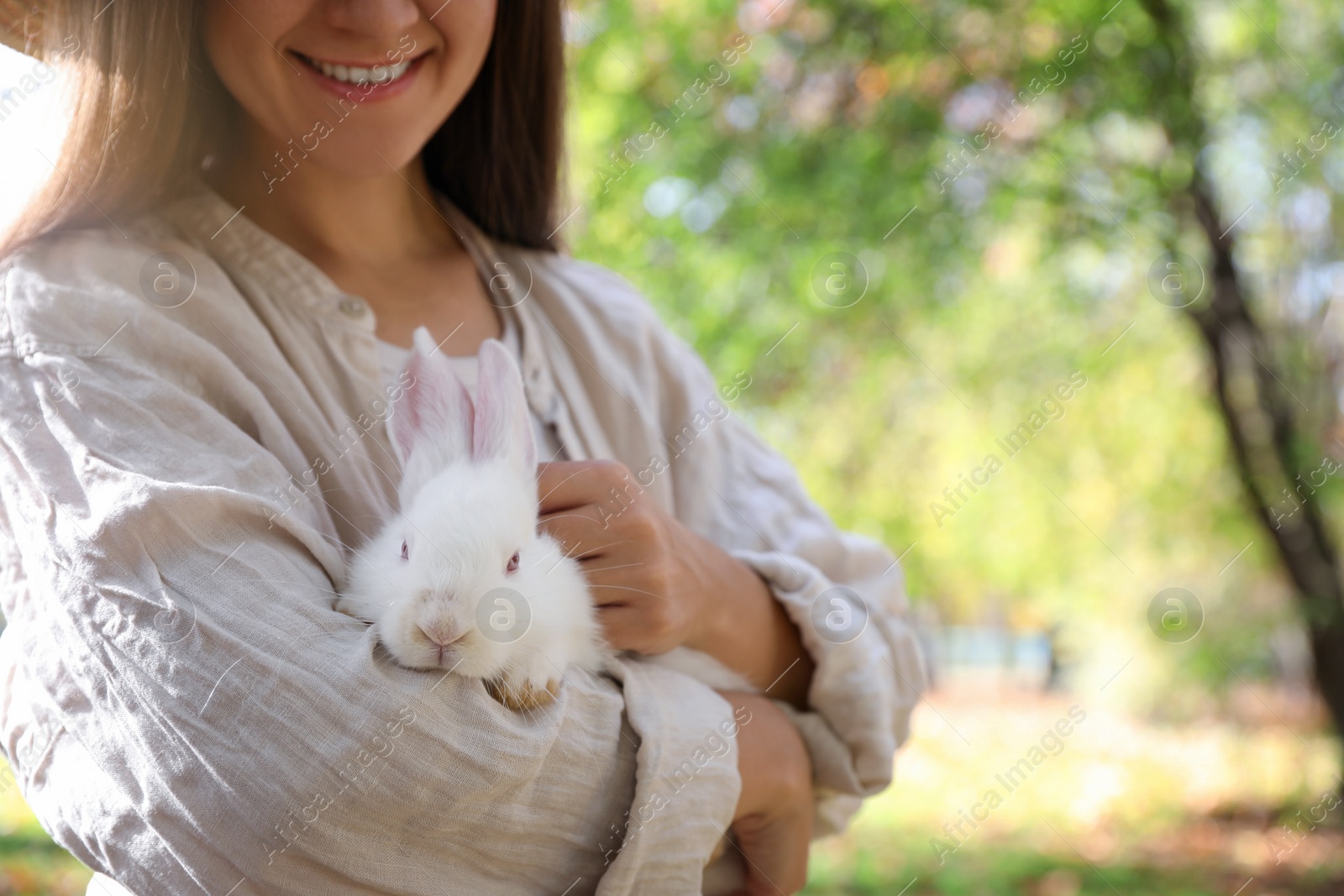 Photo of Happy woman holding cute white rabbit in park, closeup. Space for text