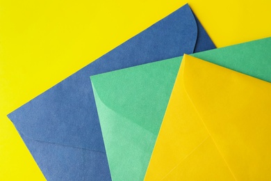 Colorful paper envelopes on yellow background, top view