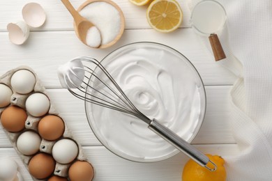 Bowl with whipped cream, whisk and ingredients on white wooden table, flat lay