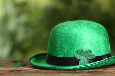 Photo of Leprechaun hat with clover leaf on wooden table against blurred background, space for text. St Patrick's Day celebration