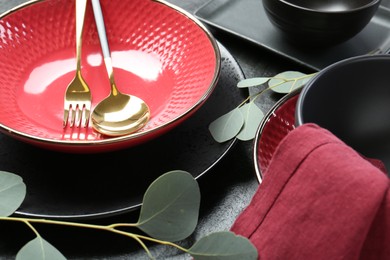 Stylish ceramic plates, cutlery and floral decor on grey table, closeup