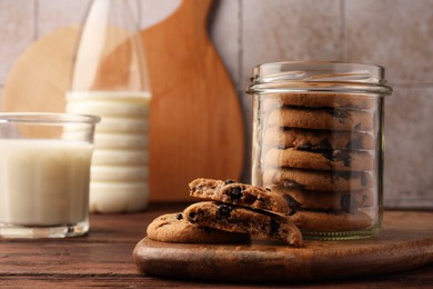 Photo of Glass jar with delicious chocolate chip cookies and milk on wooden table. Space for text