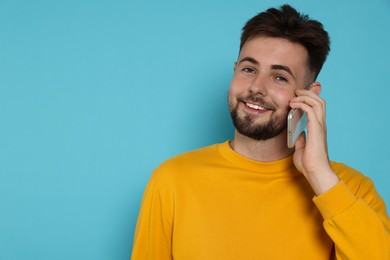 Handsome man in yellow sweatshirt talking on phone against light blue background, space for text