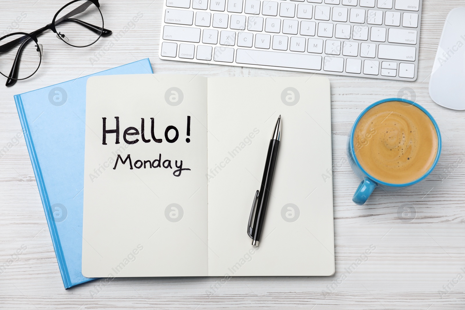 Photo of Message Hello Monday written in notebook, computer keyboard and cup of coffee on white wooden desk, flat lay